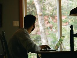 homem sentado no escritório de casa diante de computador olhando pela janela